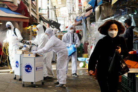Mujer llevando mascarilla reacciona ante empleados de servicio de desinfección en Seul, Sur Korea.